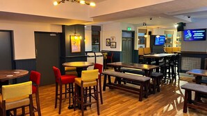 A restaurant with wooden tables and chairs, a bar area, and a television displaying a karaoke event. - The Hoptimist  (Stockton-on-Tees)