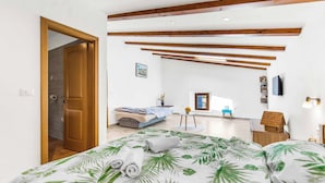A bedroom with a bed, wooden beams, a small table, a chair, and a TV.