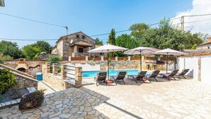 A stone pool area with lounge chairs and umbrellas, a stone building, and a view of the pool.