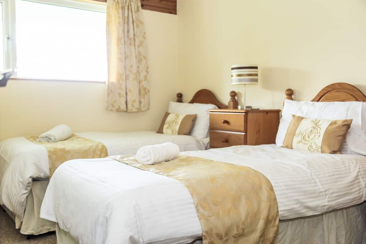 A hotel room with two beds, a wooden headboard, a nightstand, and a lamp.