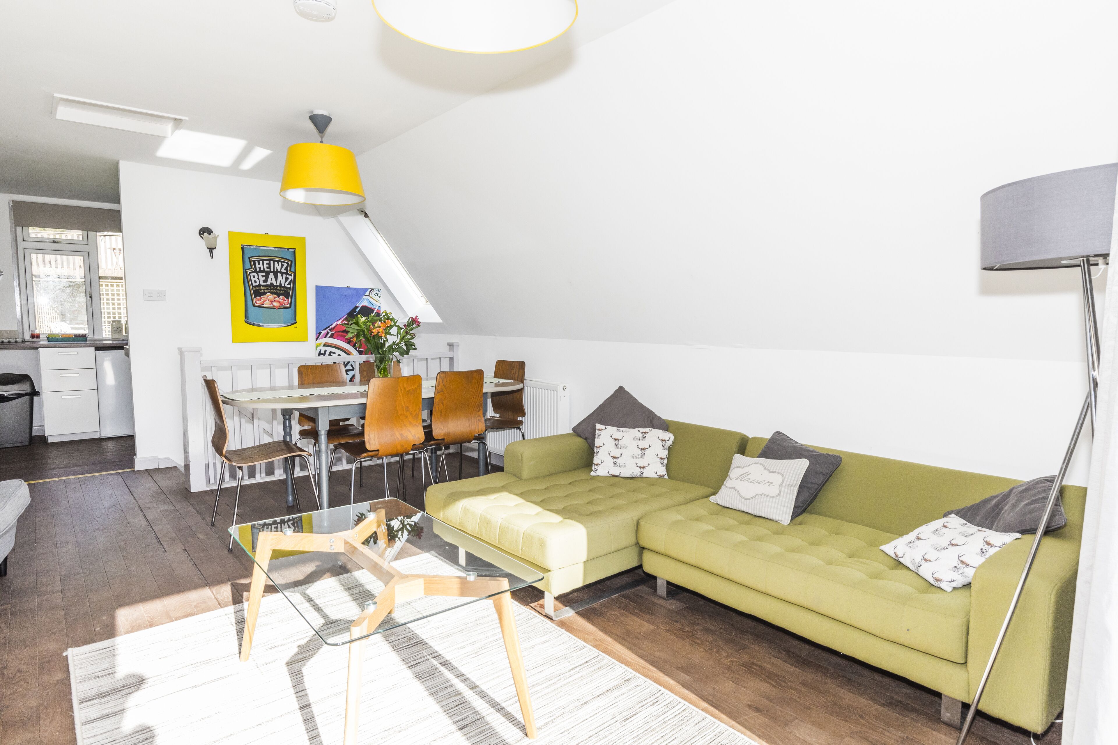 A modern living room with a green sofa, a dining table, and a yellow pendant light.