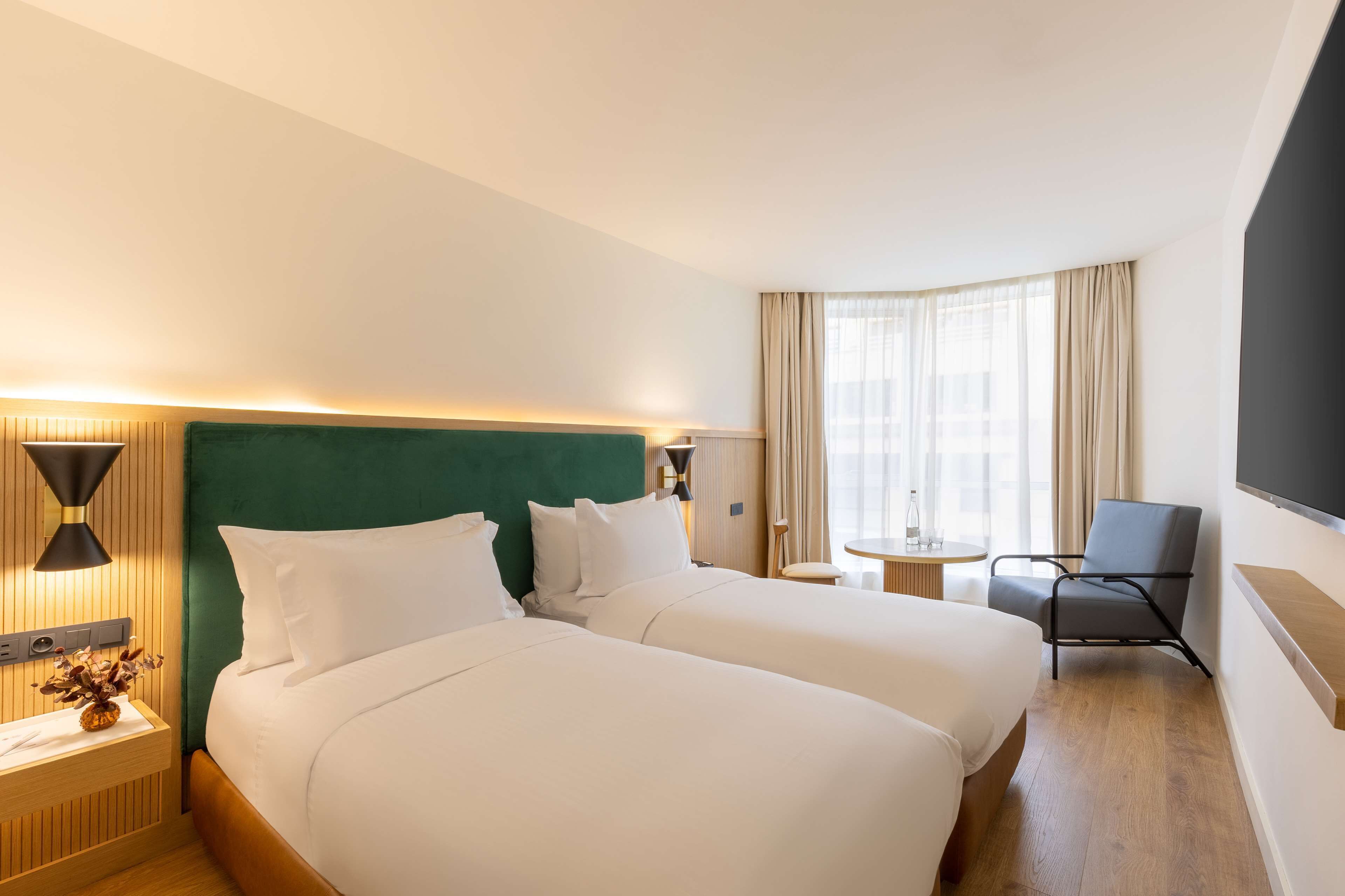 A hotel room with two beds, a desk, a chair, and a TV.