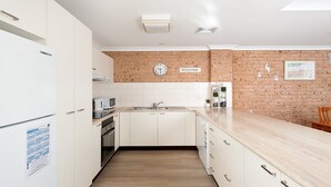 A modern kitchen with white cabinetry, a brick accent wall, a clock, and a welcome sign. - Bombora Walking Distance to Fingal Beach- Farm Rd, Fingal Bay (Fingal Bay)