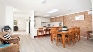A modern kitchen with white cabinets, a brick accent wall, and a dining area with wooden chairs and a table. - Bombora Walking Distance to Fingal Beach- Farm Rd, Fingal Bay (Fingal Bay)