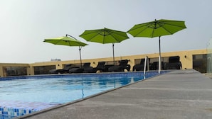 A swimming pool with three green umbrellas, lounge chairs, and a tiled edge. - Rosemond Al Hamra (Jeddah)