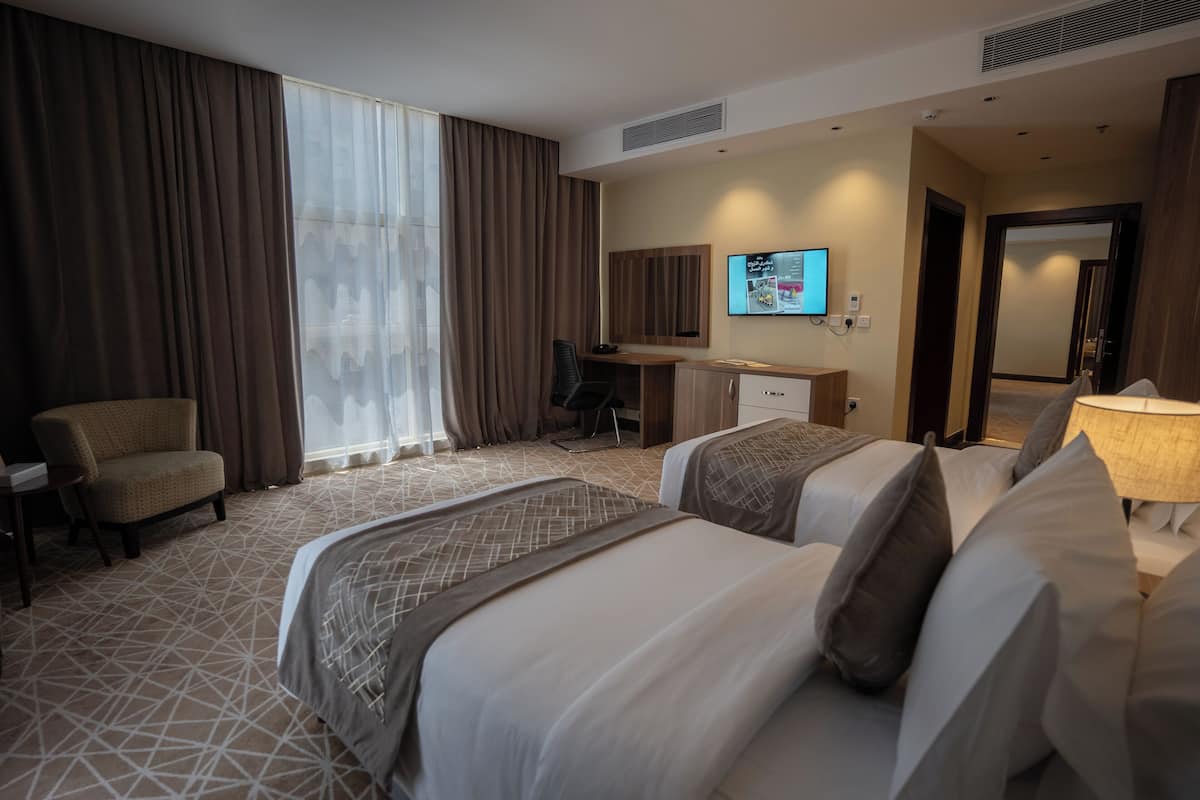 A hotel room with two beds, a desk, a chair, and a television.