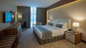 A hotel room with a large bed, bedside tables, a desk with a flat-screen TV, a chair, and a view of the outdoors through the window. - Rosemond Al Hamra (Jeddah)