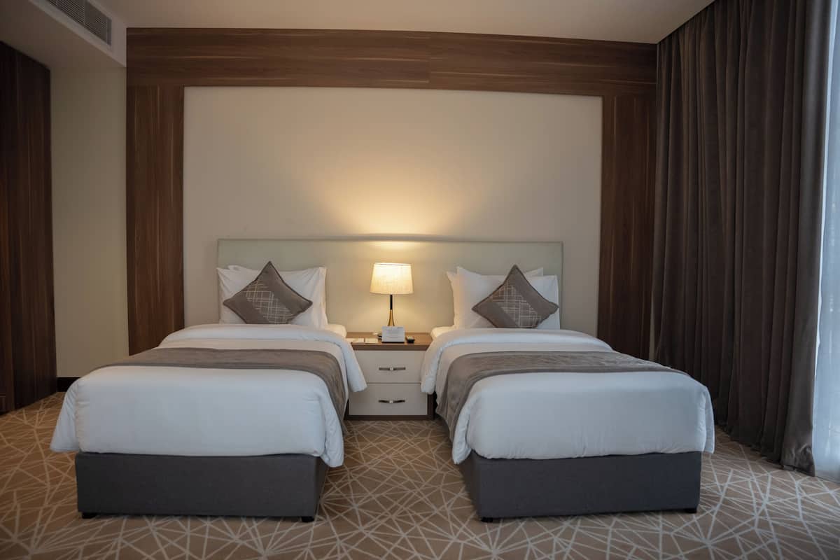 A hotel room with two beds, a nightstand with a lamp, and a geometric patterned carpet.