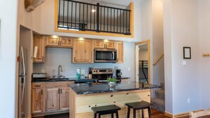 A modern kitchen with wooden cabinets, a stainless steel refrigerator, a microwave, and a large island with bar stools. - 2BR Riverside Cabin - Near Trails w/Hot Tub Access (Breckenridge)