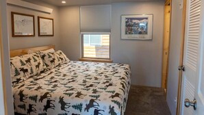 A bedroom with a bed, a window with blinds, and framed pictures on the wall. - 2BR Riverside Cabin - Near Trails w/Hot Tub Access (Breckenridge)