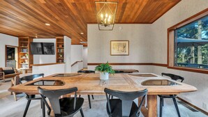 A modern dining area with a large wooden table, black chairs, a potted plant, and a large window offering a view of trees. - Talmont Pines 4BR Retreat with HOA Beach Access! (Tahoe City)