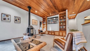 A cozy living room with a wooden ceiling, a fireplace, a bookshelf, and a comfortable seating area.