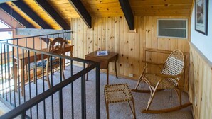 Uma cabana de madeira com varanda, equipada com uma mesa, cadeiras e uma cadeira de balanço.