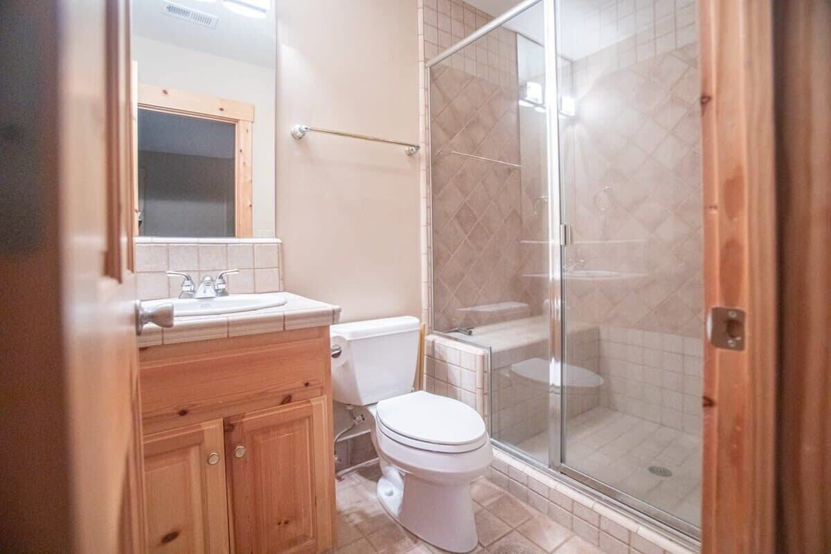 A bathroom with a wooden vanity, a white toilet, and a glass-enclosed shower area.
