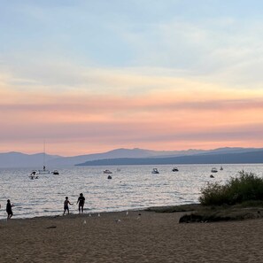 A beach with boats on the water and people on the shore.