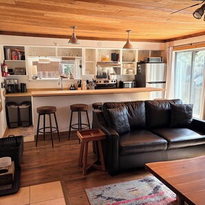 A modern kitchen with wooden cabinets, a central island, and a black leather sofa.
