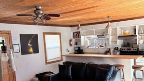 Una sala de estar acogedora con un sofá de cuero negro, una mesa de centro de madera y un ventilador de techo.