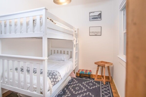 Habitación con literas, una ventana, un taburete de madera y una alfombra estampada.