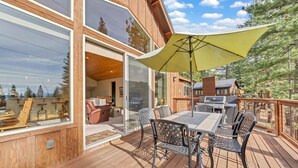Eine Holzterrasse mit Gartenmöbeln, einem Grill und einem großen Sonnenschirm, der Schatten spendet.