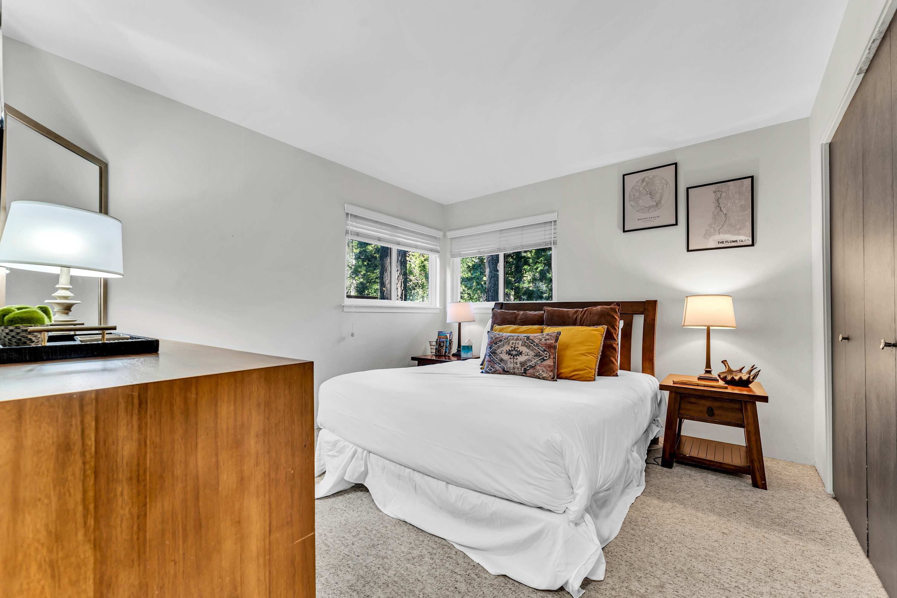A bedroom with a bed, bedside tables, a dresser, and two windows.