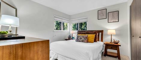A bedroom with a bed, bedside tables, a dresser, and two windows.