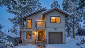 A two-story house with a front porch, a garage, and a snow-covered landscape. - Tahoe Vista Retreat with Lake View- Walk to beach! (Tahoe Vista)