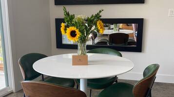 Un coin repas avec une table ronde blanche, quatre chaises vertes et un vase rempli de tournesols.