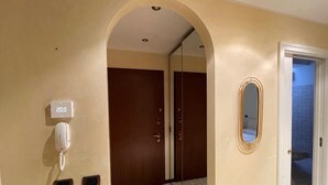Un pasillo de hotel con un teléfono, un espejo y una puerta que da a otra habitación.
