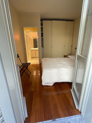 A bedroom with a bed, wooden flooring, a wardrobe, and a small seating area.