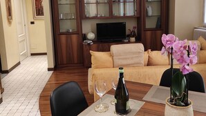 Una sala de estar con un mueble de televisión de madera, un sofá, una mesa de comedor con dos sillas y una orquídea en maceta.