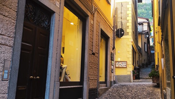 Una estrecha calle adoquinada bordeada por edificios con grandes ventanales y puertas, algunos con balcones.