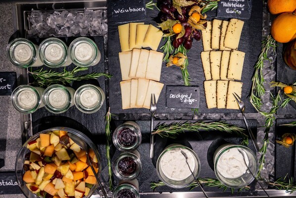 A cheese and fruit platter with various cheeses and fruits on a slate board. - Wedina Serviced Apartments (Hamburg)