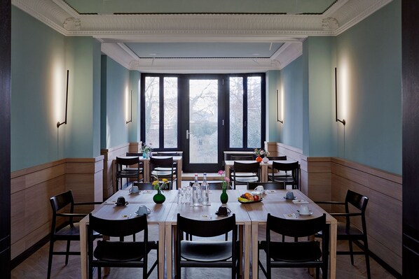 A dining area with a long table set for six, flanked by tall windows and wall-mounted lights. - Wedina Serviced Apartments (Hamburg)