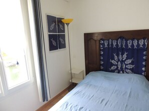 Un dormitorio con cama, mesita de noche, lámpara y ventana con cortinas.