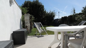 An outdoor patio with a white table and two lounge chairs, a black speaker, and a concrete wall.