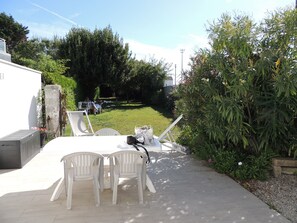 Un patio con sillas y una mesa de plástico blanco, rodeado de follaje y un muro de piedra.