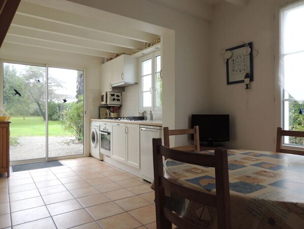 Una cocina con puerta corrediza de vidrio que da a un jardín, lavadora, microondas y televisor sobre una mesa.