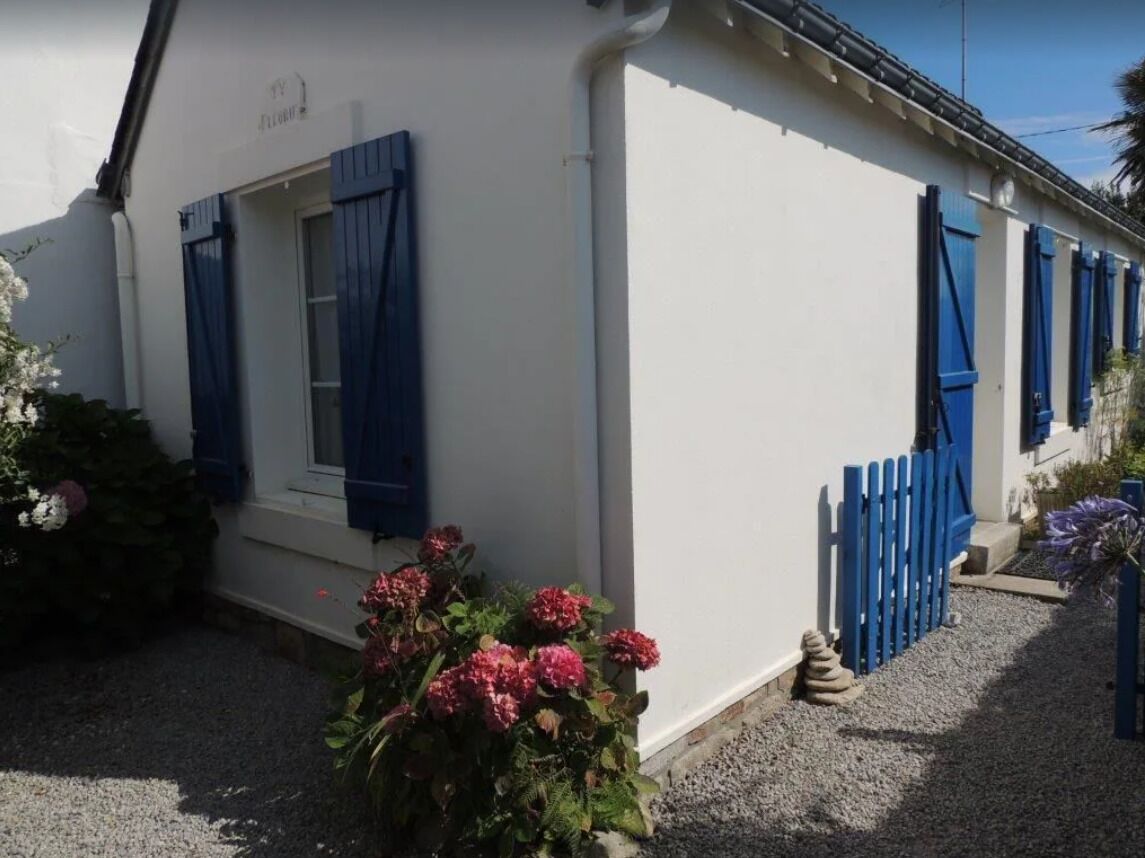 A white building with blue shutters, a gravel driveway, and a blue fence.