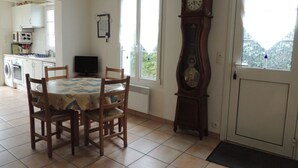 A dining area with a table and chairs, a clock, and a view through a door.