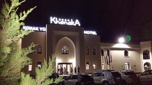 A hotel named "Khanaka" with a prominent sign, a parking lot with several cars, and a building with arched windows and a central entrance. - Hotel Khanaka (Turkestan)