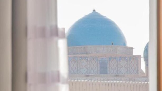 A room with a view of a large blue dome structure through a window. - Hotel Khanaka (Turkestan)