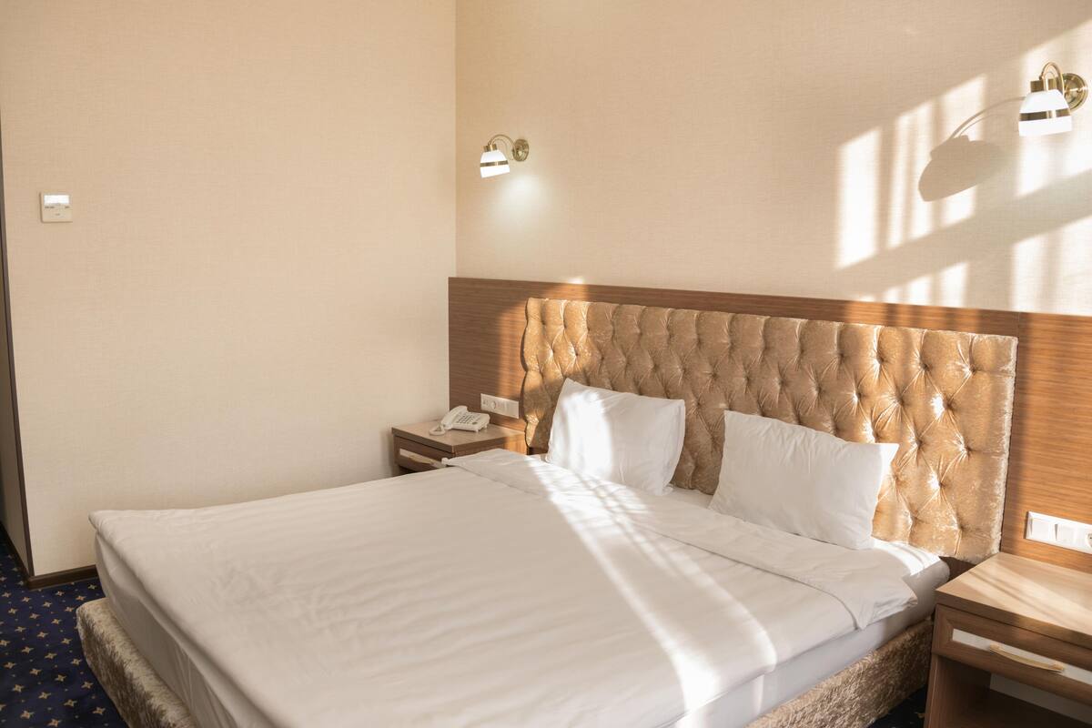 A neatly made bed with a tufted headboard, a bedside table with a lamp, and a wall-mounted light fixture.