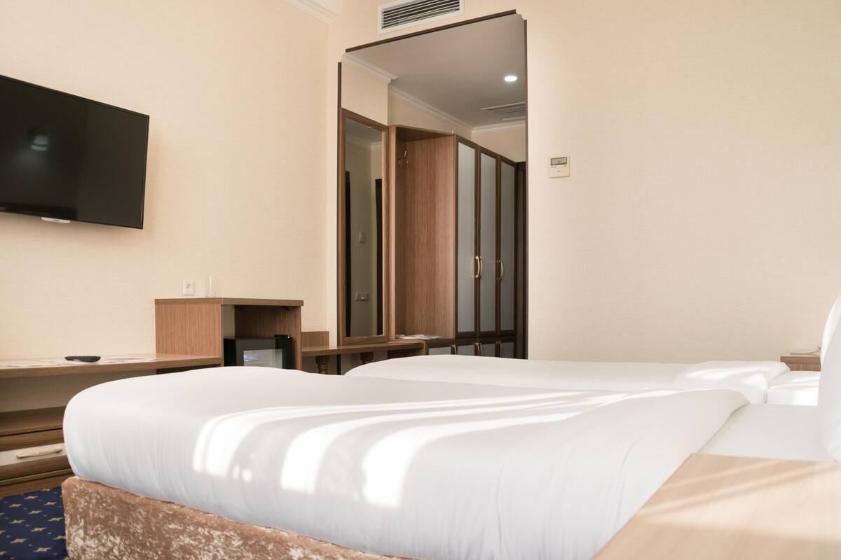 A hotel room with a large bed, a TV mounted on the wall, and a mirror reflecting the room.