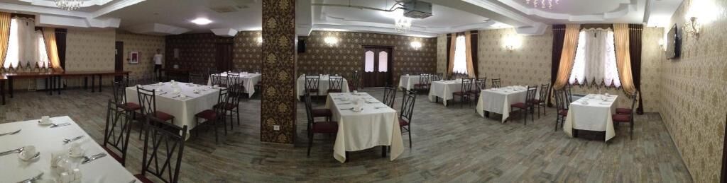 A banquet hall with multiple round tables and chairs, a central pillar, and patterned wallpaper.