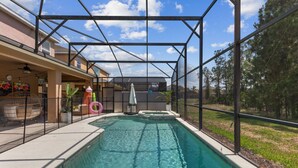 Une piscine extérieure dotée d’une structure en verre, entourée d’une terrasse aménagée avec des sièges et des plantes en pot.