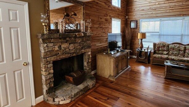 A cozy living room with a stone fireplace, wooden walls, a sofa, and a television.