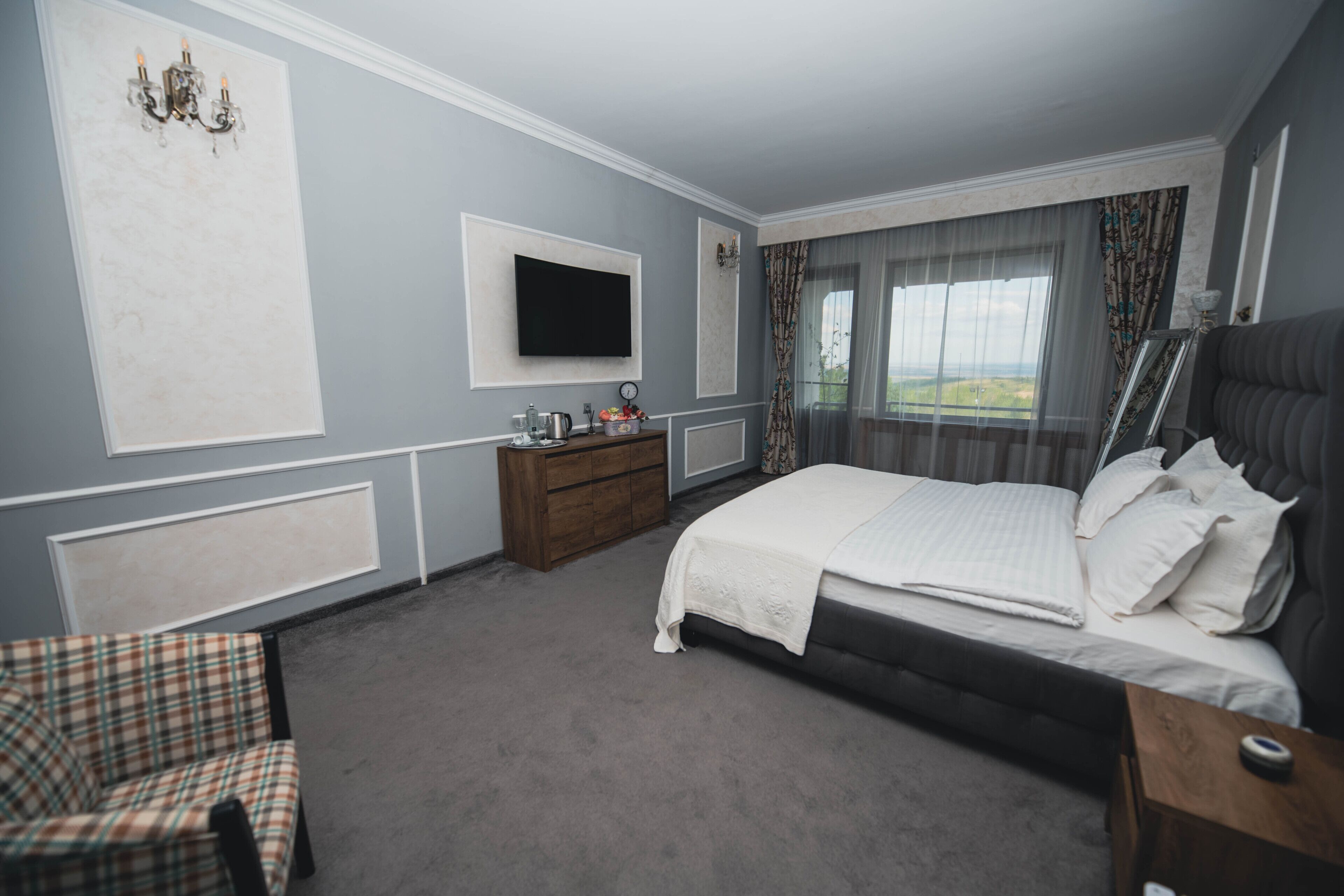 A bedroom with a large bed, a television mounted on the wall, a wooden dresser, and a chair.