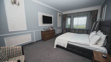 A bedroom with a large bed, a television mounted on the wall, a wooden dresser, and a chair.