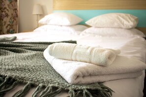 A neatly made bed with white linens and a folded green blanket.