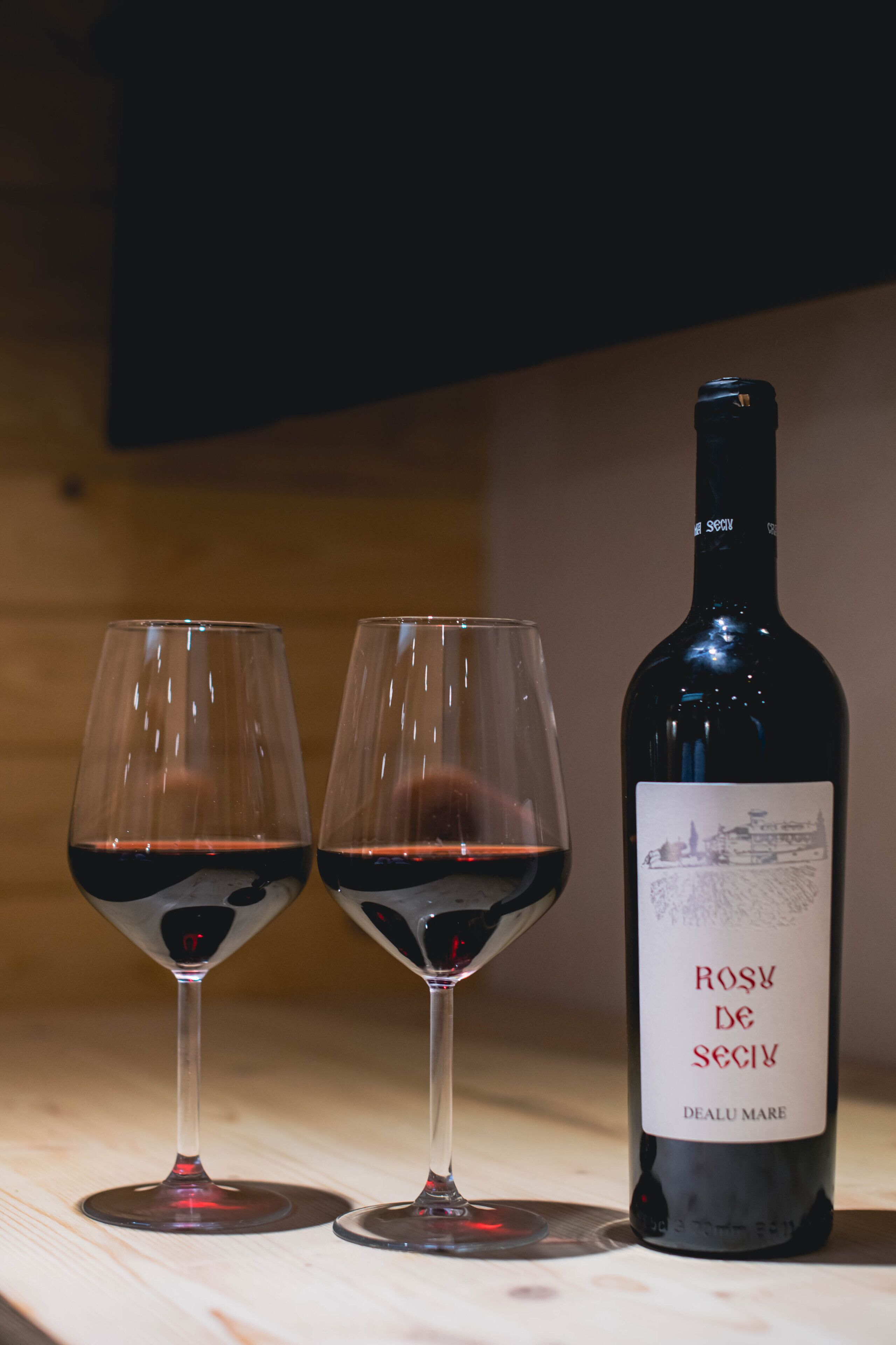 Deux verres à vin remplis de vin rouge et une bouteille de vin Rosy de Secy, le tout posé sur une surface en bois.